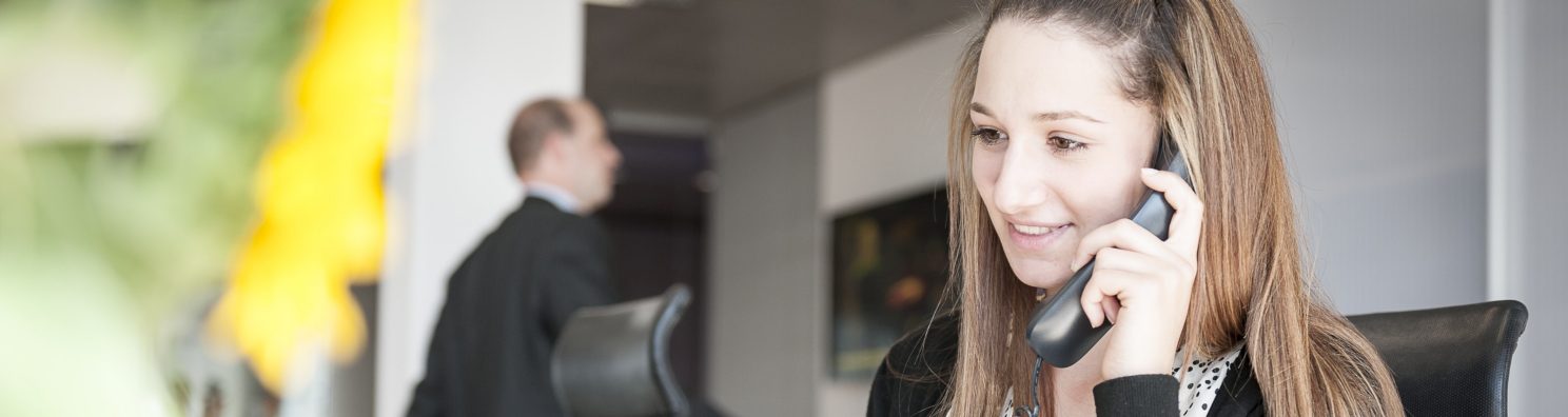 Young woman at reception desk holding telephone
